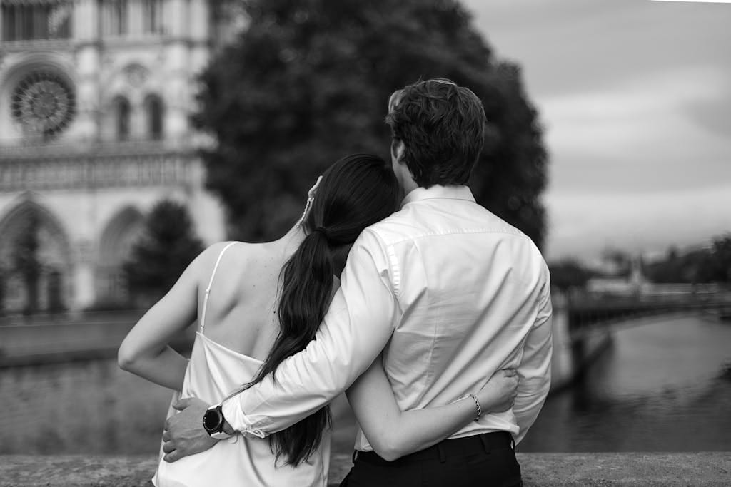 A black and white photo of a couple embracing with Notre Dame in the background.