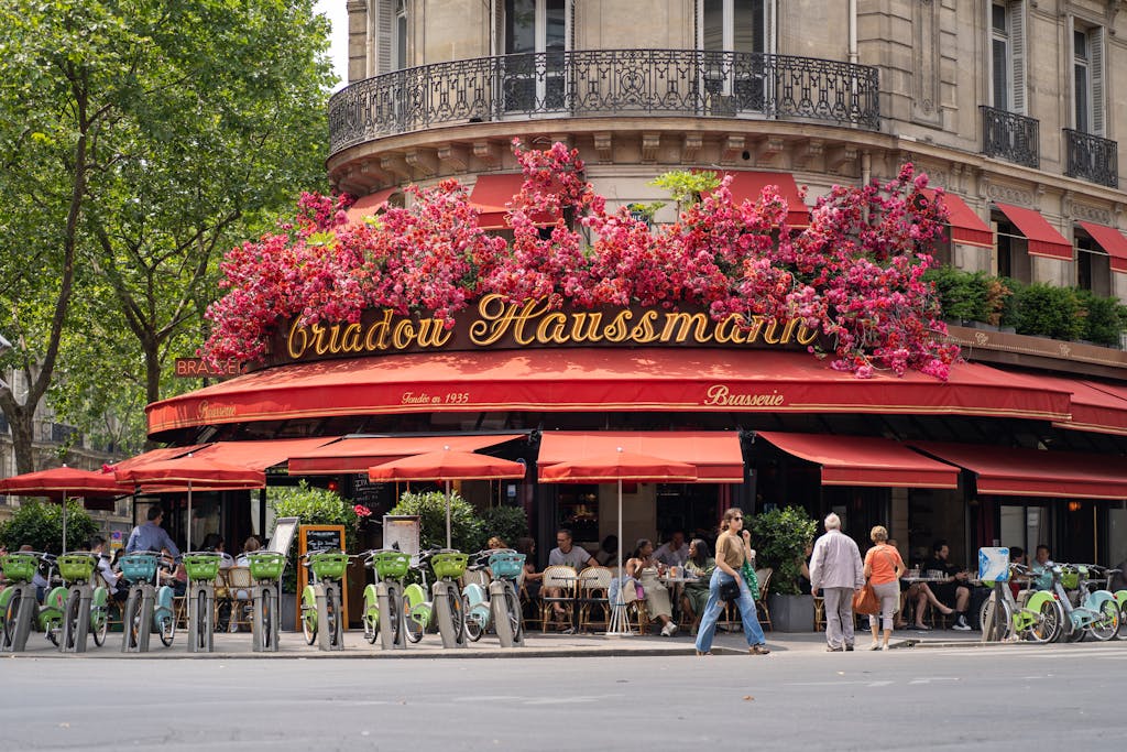 Parisian brasserie with vibrant flowers and outdoor seating, lively scene.