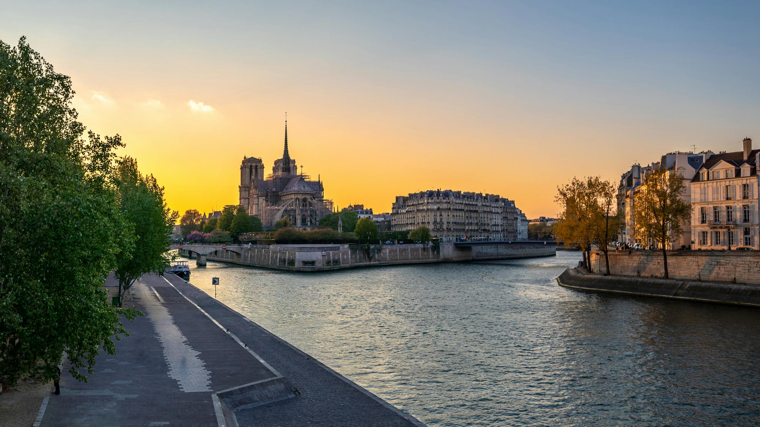 Captivating sunset view of Notre Dame de Paris with calm river and cityscape in the background.