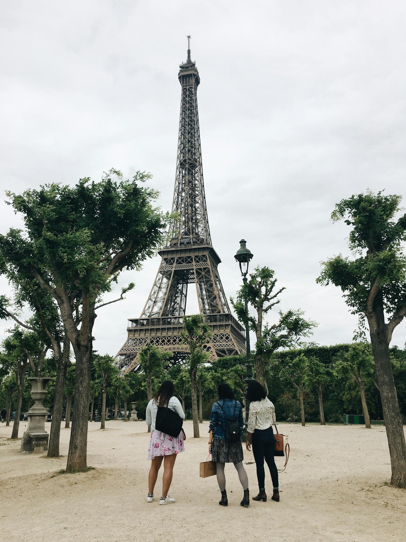 Three tourists admire the Eiffel Tower from a nearby park in Paris, perfect for travel and tourism themes.